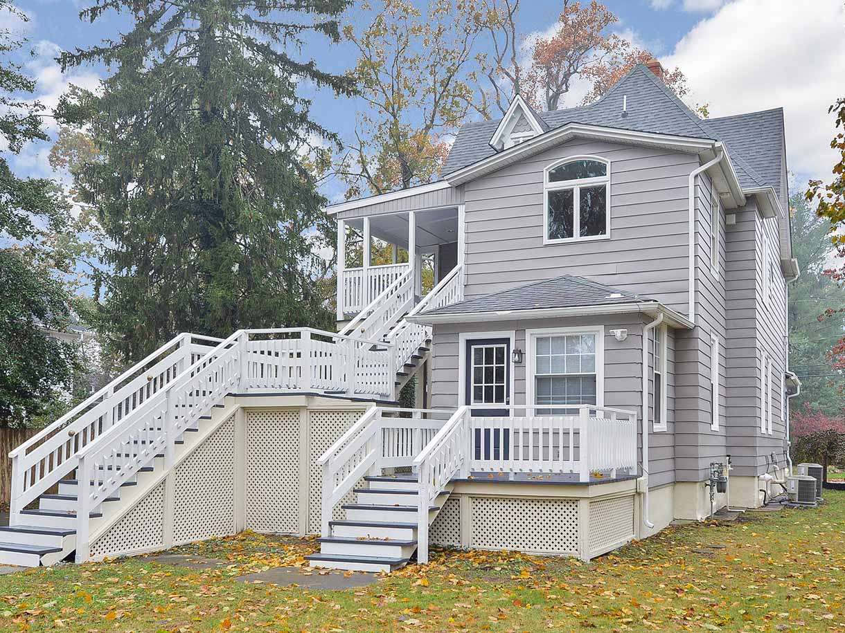 Backyard view of a grey house with two staircases leading into the yard from two balcony areas