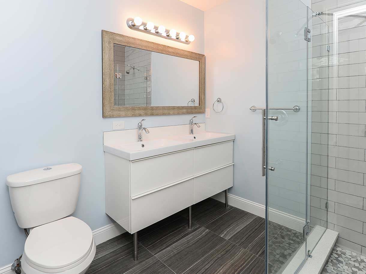 Bathroom with light blue walls, shower, double sink and toilet