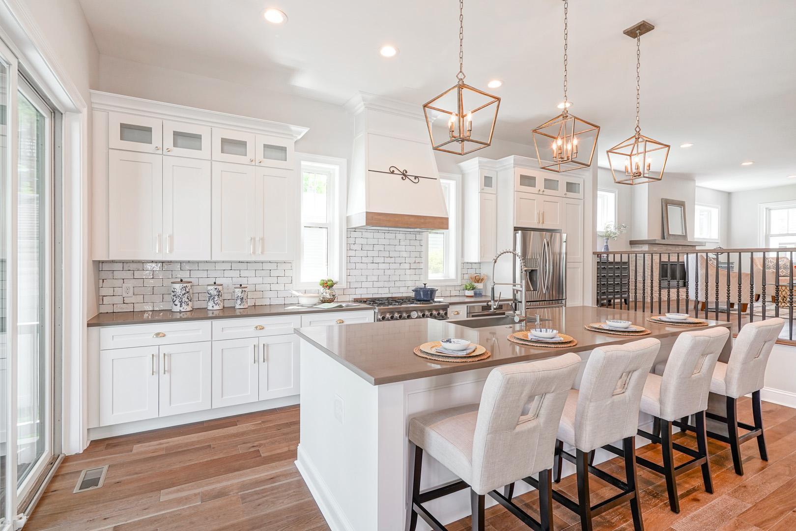 Kitchen with designed backsplash tiles, island with modern black stools, and white cabinets